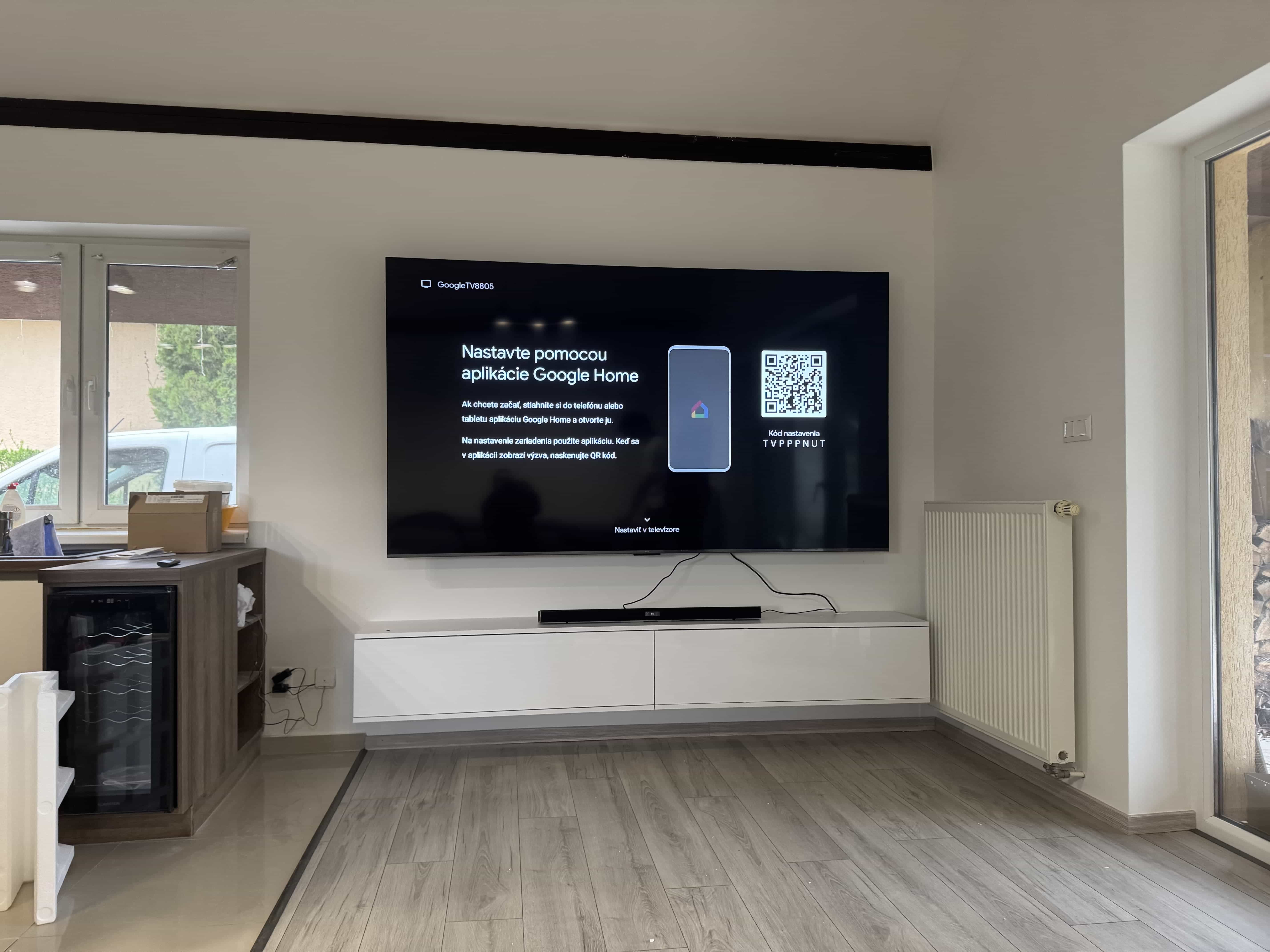 Veľký televízor so soundbarom na bielej zostave, Google TV